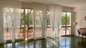 A spacious room with large windows covered by sheer curtains, a tiled floor, and a table with chairs outside. - 4 Bedroom Villa in Marsala (Marsala)