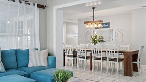 Una sala moderna con un sofá azul, un comedor con sillas blancas y una mesa de madera.