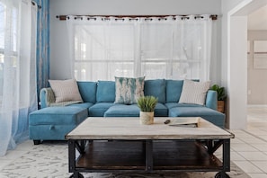A living room with a blue sectional sofa, a wooden coffee table, and a potted plant.