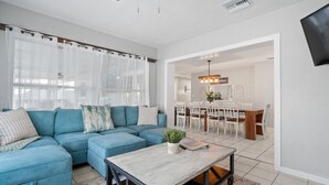 Una sala moderna con un sofá seccional azul, una mesa de centro y un comedor con candelabro.