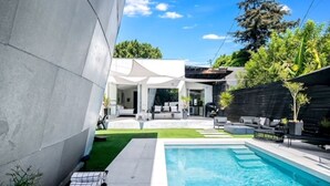 A modern outdoor pool area with a clear blue pool, a white canopy, and a well-maintained lawn.