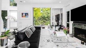 A modern living room with a black leather sofa, a glass coffee table, and a fireplace.