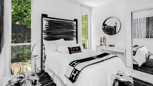 A modern bedroom with a large bed, a round mirror, and a view of greenery outside.