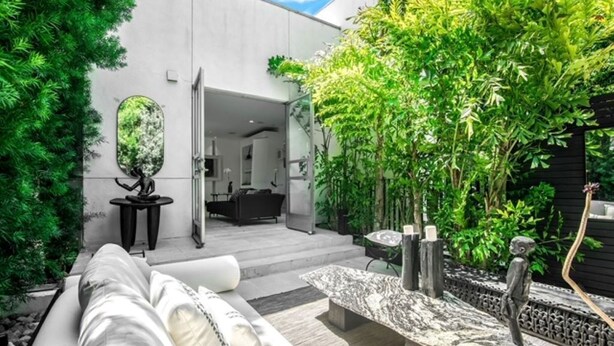 A modern outdoor living area with a sofa, a stone table, and a garden with various plants and a sculpture.
