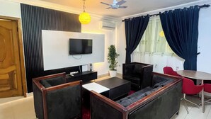 Una sala de estar con un sofá, un televisor, un ventilador de techo y una mesa de comedor con sillas.