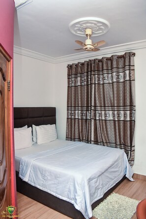 Cozy retreat with a neatly made bed, ceiling fan, and patterned curtain.