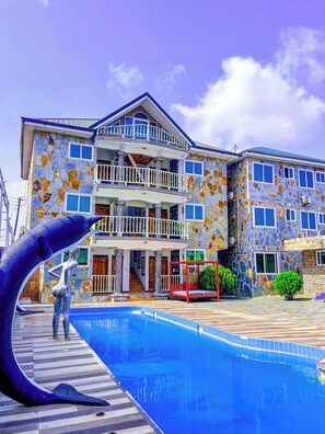 A multi-story building with a stone facade, a swimming pool, and a statue. - RK Italian Boy Hotel (Accra)