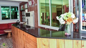 Un área de recepción con mostrador de madera, un florero de cristal con flores, un sofá rojo y un ventanal grande.