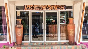 Entrada de un hotel con un cartel que dice 'Welcome to RK Italian Hotel', dos jarrones grandes y un área de recepción visible a través de las puertas de vidrio.