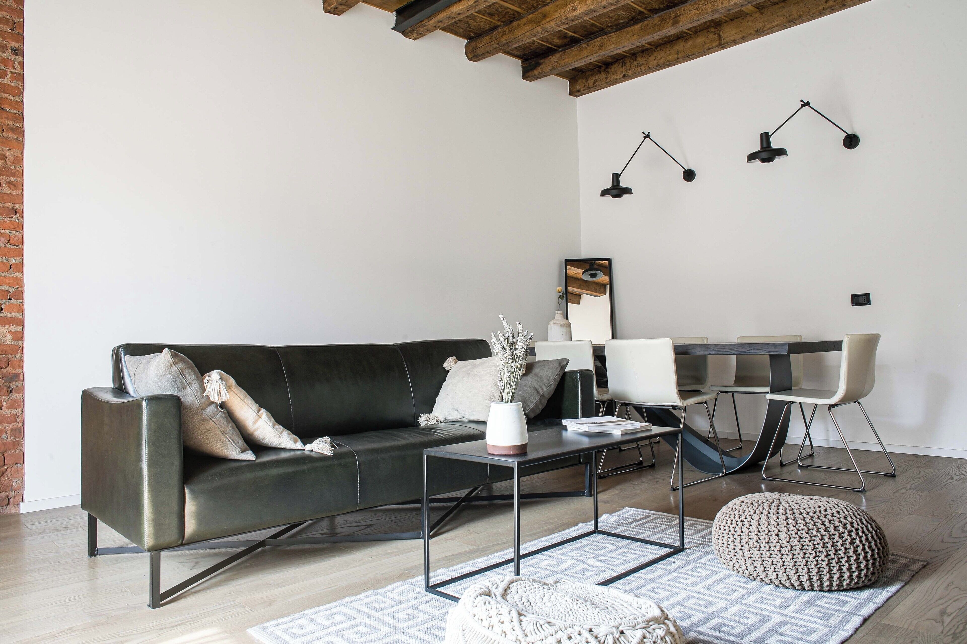 A modern living room with a dark leather sofa, a coffee table, and a dining area with a white table and chairs.