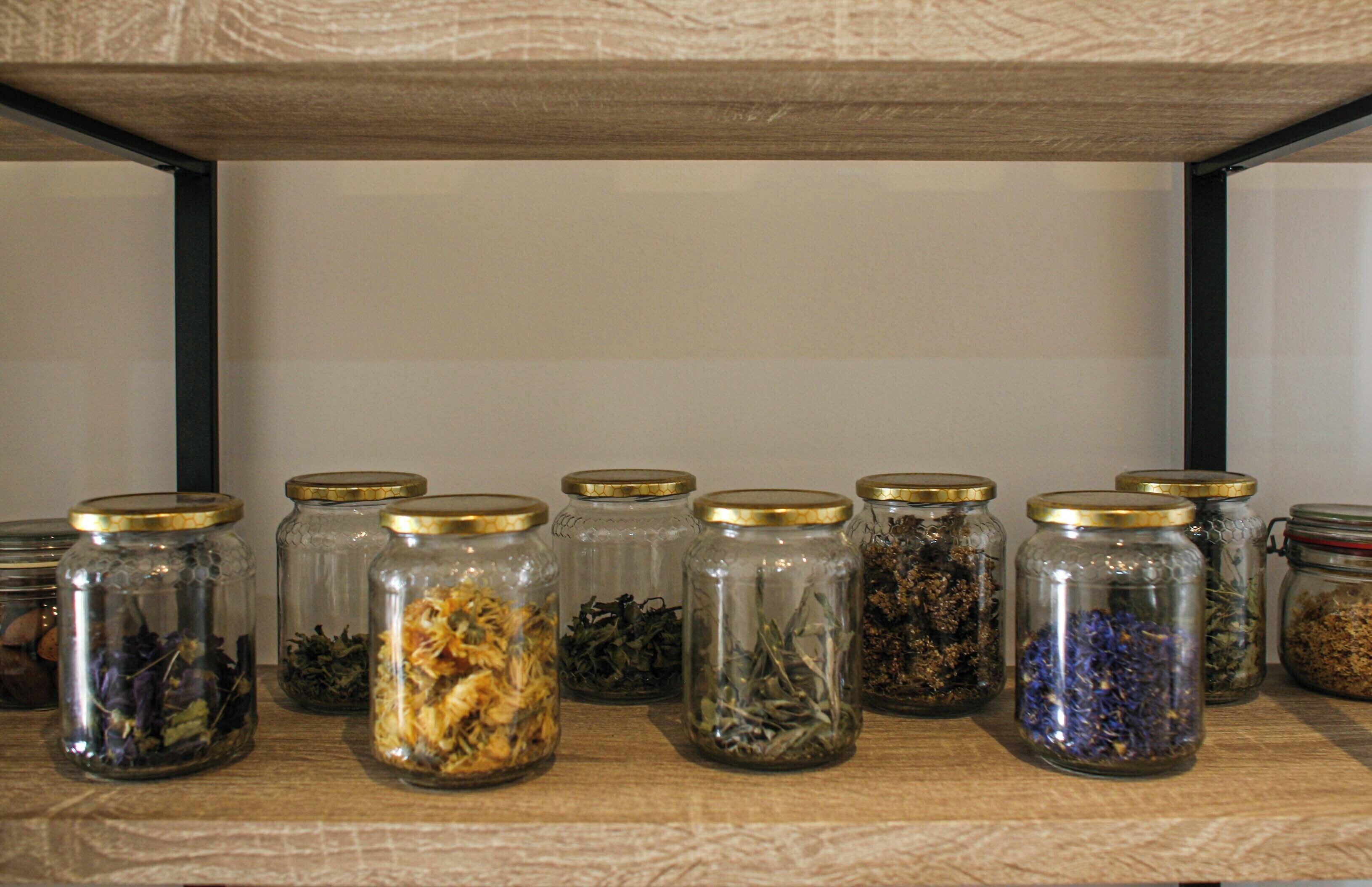 A shelf with multiple glass jars containing various dried herbs and flowers.