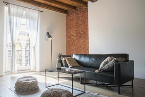 A modern living room with a black leather sofa, a glass coffee table, and a brick wall. - BnButler - Buenos Aires 51 (Milan)