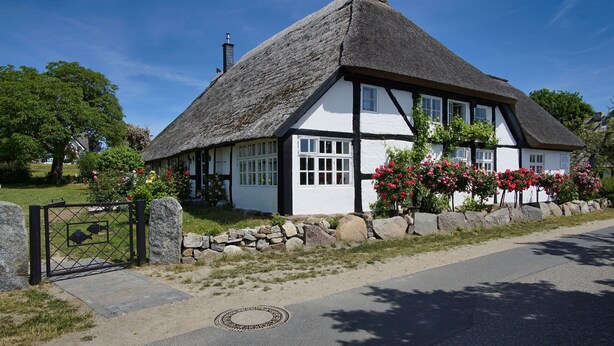 Ein traditionelles Reetdachhaus mit einer Steinmauer und einem Metalltor.