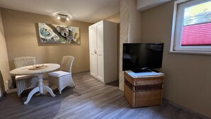Un espacio habitable compacto con una mesa de comedor y sillas, un televisor sobre un mueble, un armario y una ventana con persianas.