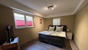 Un dormitorio con cama, televisión, mesita de noche, lámpara y ventana con persianas.
