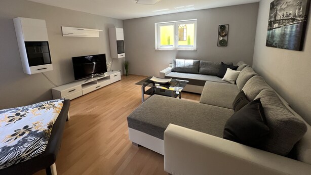 Una sala de estar moderna con un televisor de pantalla plana, un sofá, una mesa de centro y un comedor.