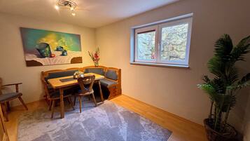A dining area with a wooden table and chairs, a painting on the wall, a window with a view, and a potted plant.