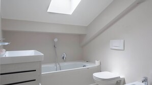 Une salle de bain moderne dotée d’un puits de lumière, d’une baignoire, de toilettes et d’un bidet.