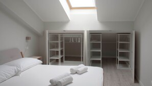Une chambre dotée d’une lucarne, d’un lit avec du linge de lit blanc et d’un dressing avec de nombreuses étagères.