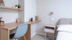Une chambre avec un bureau en bois, une chaise bleu clair, une table de chevet avec une lampe et un lit avec une literie blanche.
