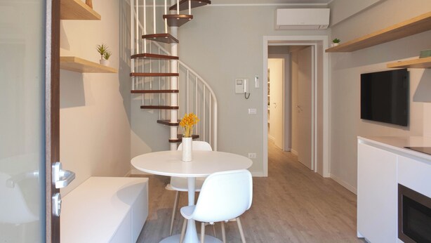 Une cuisine moderne avec des meubles blancs, un four encastré et un téléviseur noir fixé au mur, au-dessus du plan de travail.
