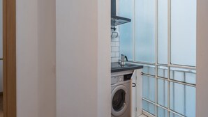 A compact kitchen with a washing machine, a coffee maker, and a window with frosted glass.
