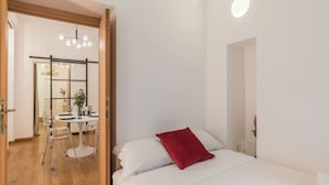 A bedroom with a bed, a red pillow, and a white wall.