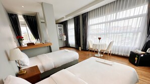 A hotel room with two beds, a desk, a chair, a table, and a large window with curtains. - The White House Rachamankha (Chiang Mai)