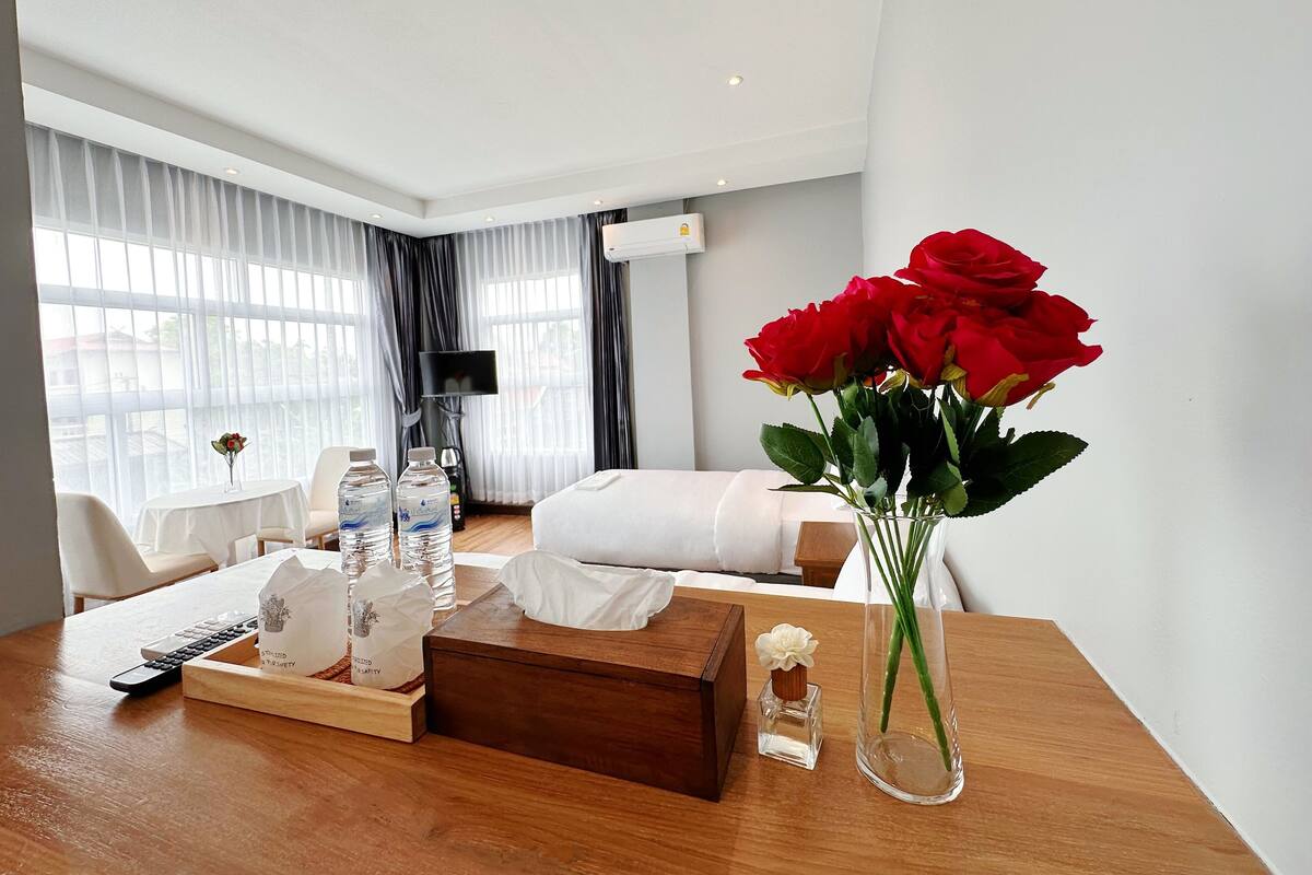 A hotel room with a wooden table, a vase of red roses, bottled water, and a remote control.