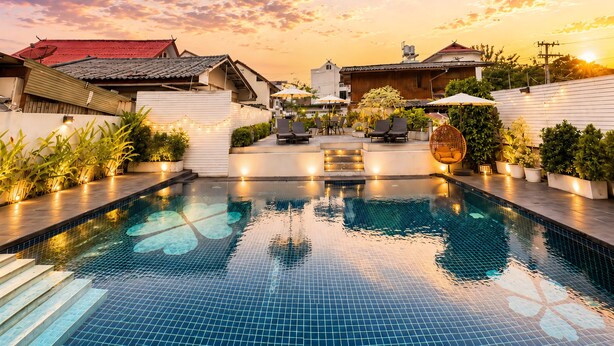 A swimming pool with tiled flooring, surrounded by outdoor seating and potted plants. - The White House Rachamankha (Chiang Mai)