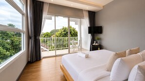 A hotel room with a large bed, a TV, and a balcony with a view of trees. - The White House Rachamankha (Chiang Mai)