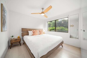 A bedroom with a wooden bed, a nightstand, a ceiling fan, a window with a view, and a door with a geometric design.