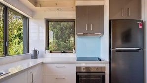 Une cuisine moderne dotée d’appareils électroménagers en acier inoxydable, de meubles blancs et d’une grande fenêtre offrant une vue sur la verdure.