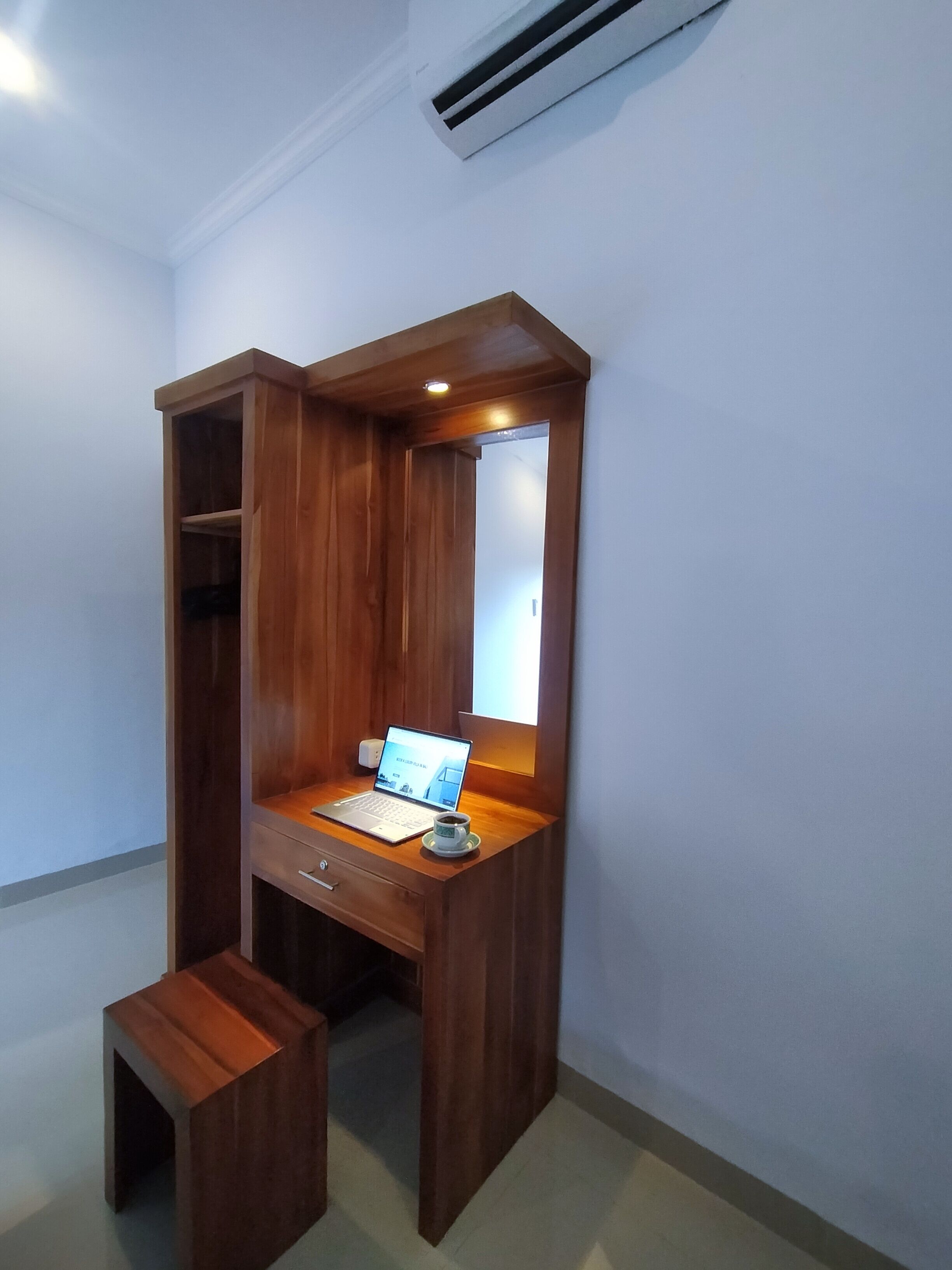 Een houten bureau met een laptop en een kop, een klein krukje en een spiegel.
