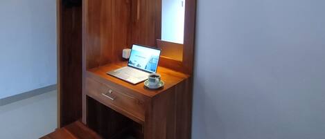 Een houten bureau met een laptop en een kop, een klein krukje en een spiegel.