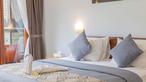 Een netjes opgemaakt bed met een handdoek in de vorm van een zwaan, een doos zakdoekjes, grijze kussens en een geborduurd sprei.