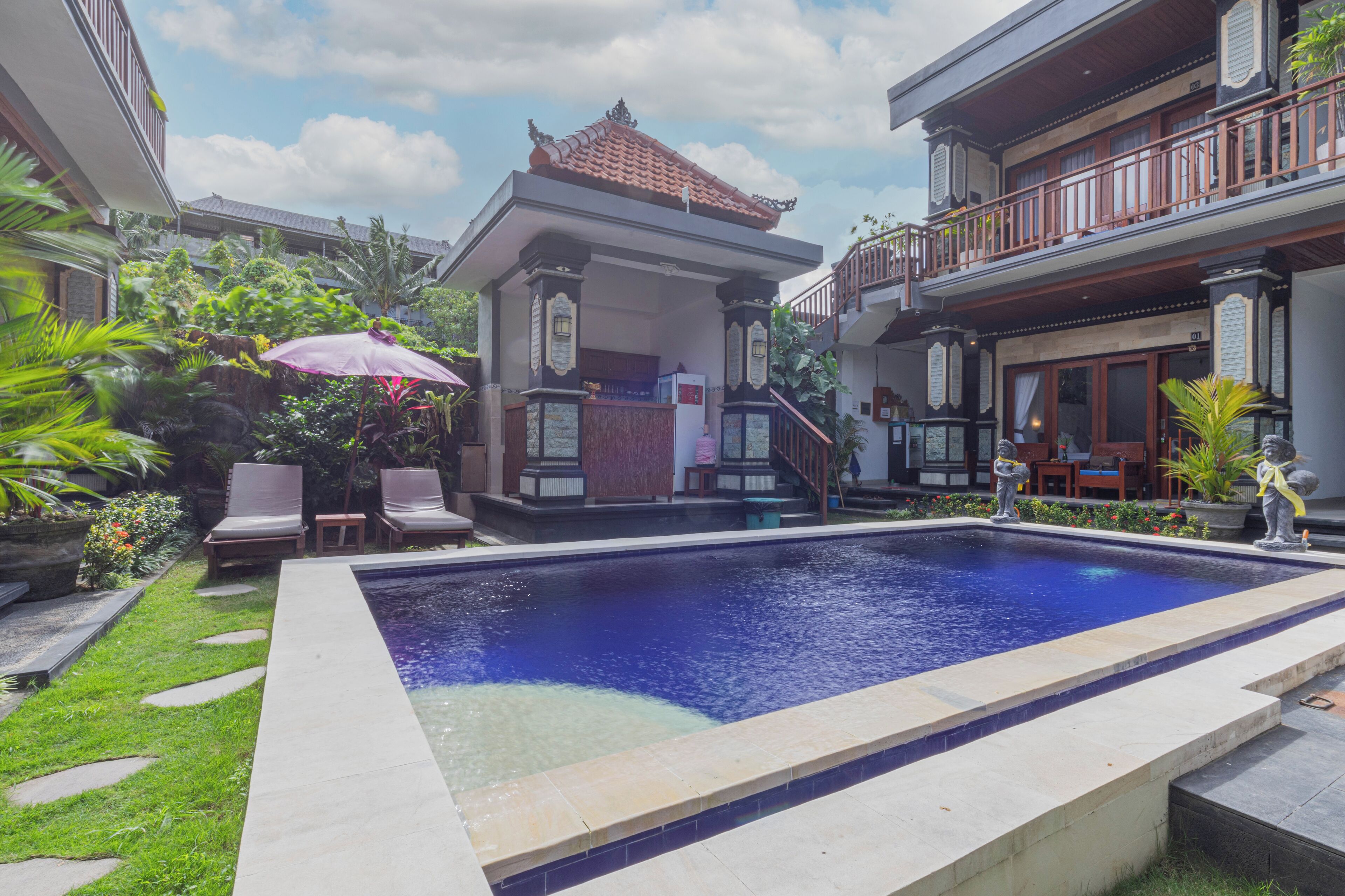 A swimming pool with a stone border, surrounded by a garden with palm trees and a gazebo.