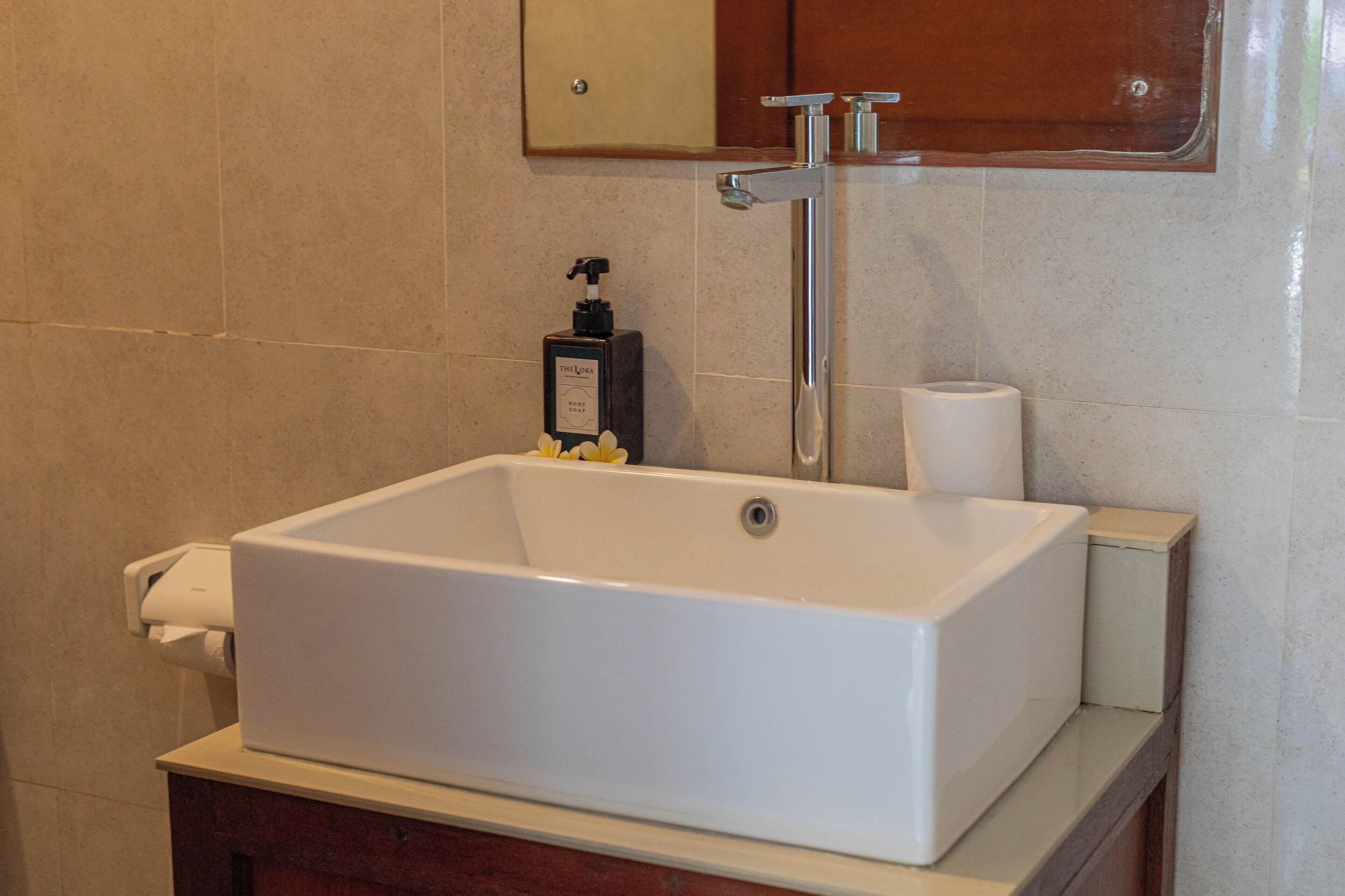 A rectangular white bathtub with a faucet and a soap dispenser on a wooden vanity.