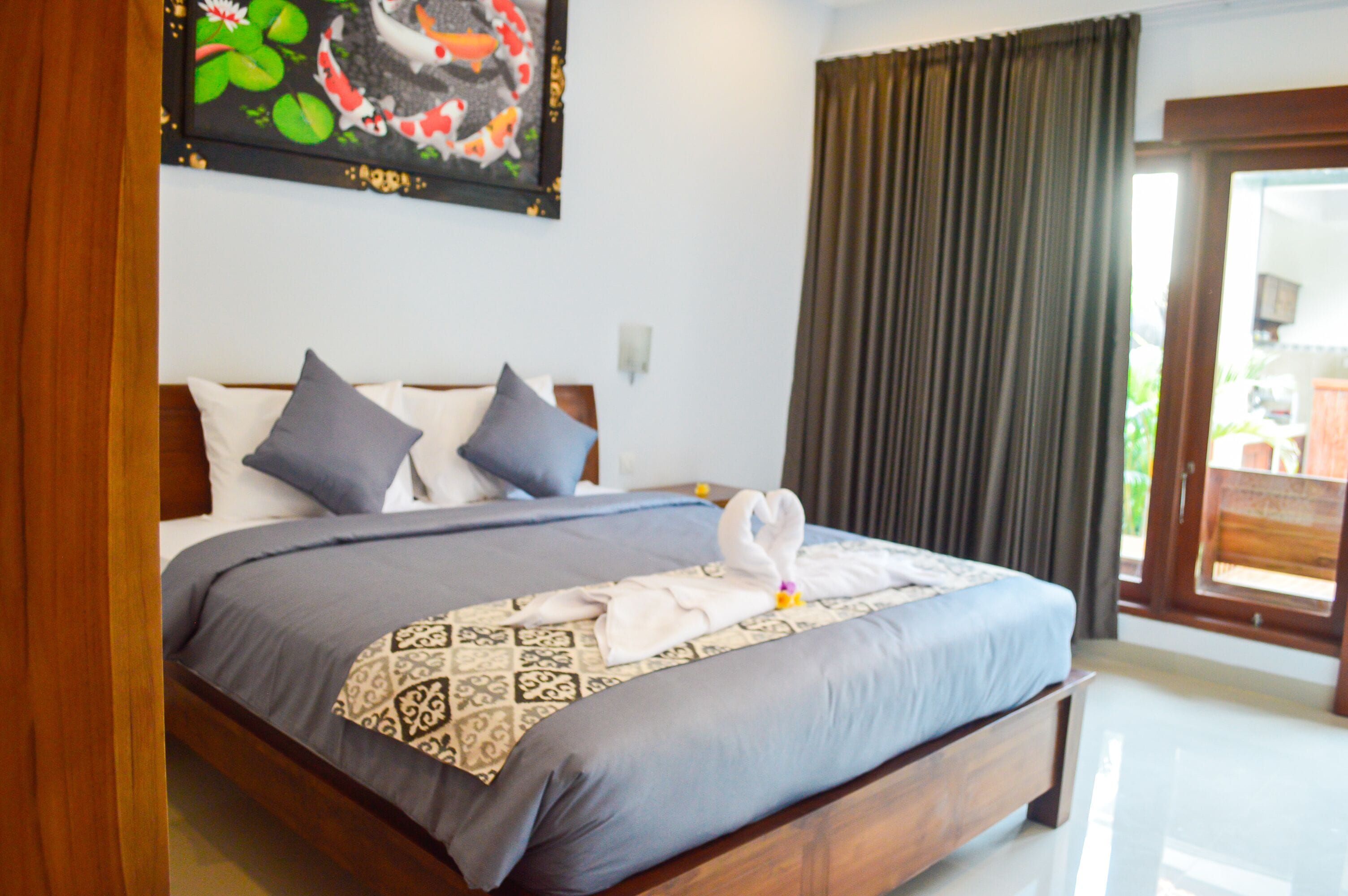Cama bem arrumada com colcha estampada, dois travesseiros e arranjo decorativo com toalhas em formato de cisne.
