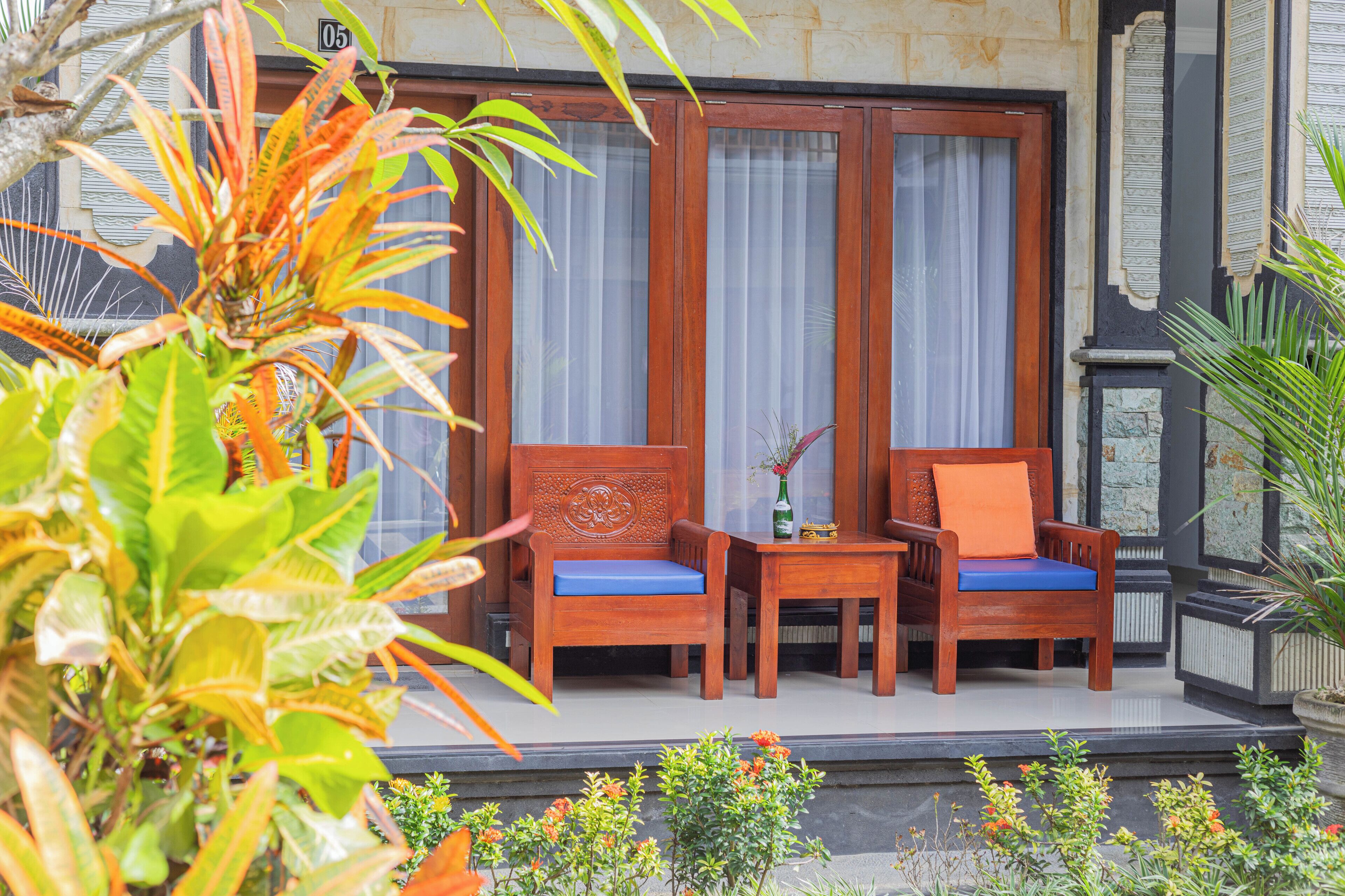 A wooden outdoor seating area with two chairs and a table, surrounded by tropical plants.