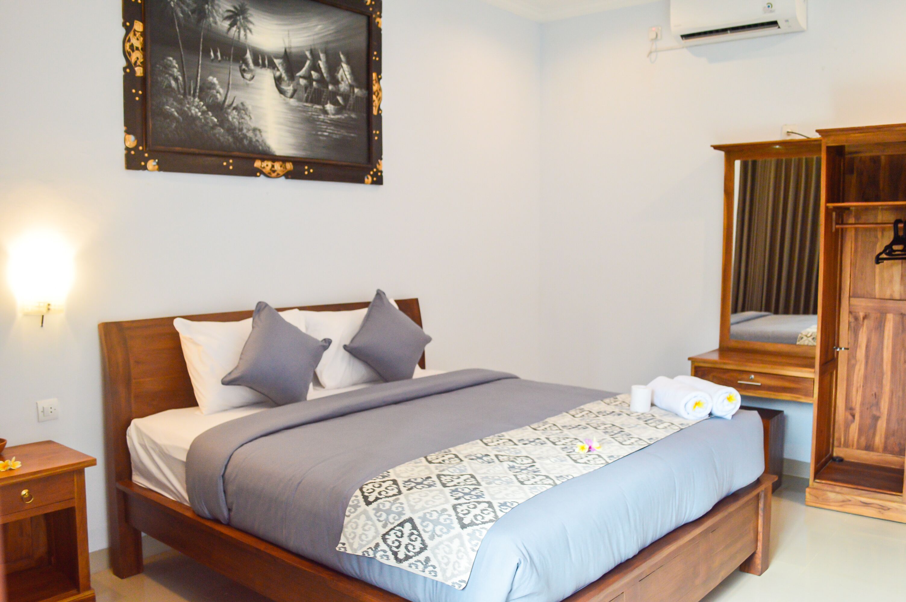 A neatly made bed with a patterned bedspread, a bedside table with a lamp, and a wardrobe with a mirror.