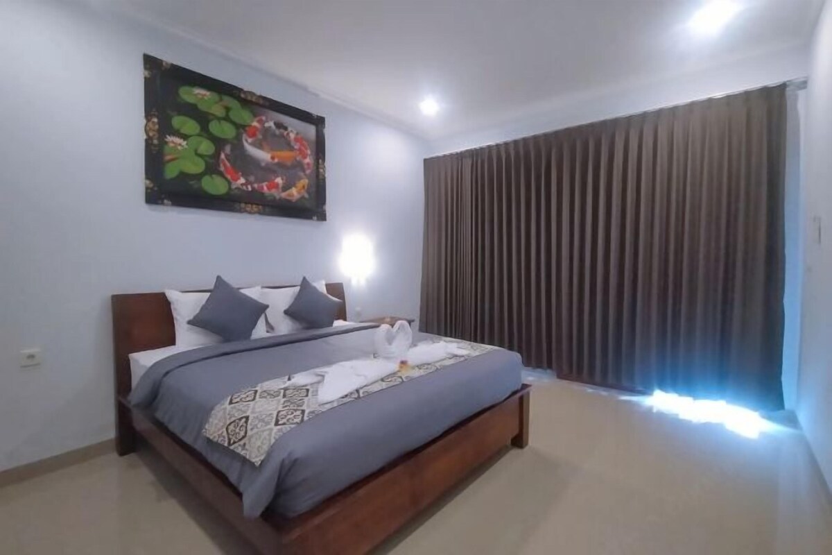A bedroom with a bed, a headboard, a wall-mounted picture, and a window with curtains.