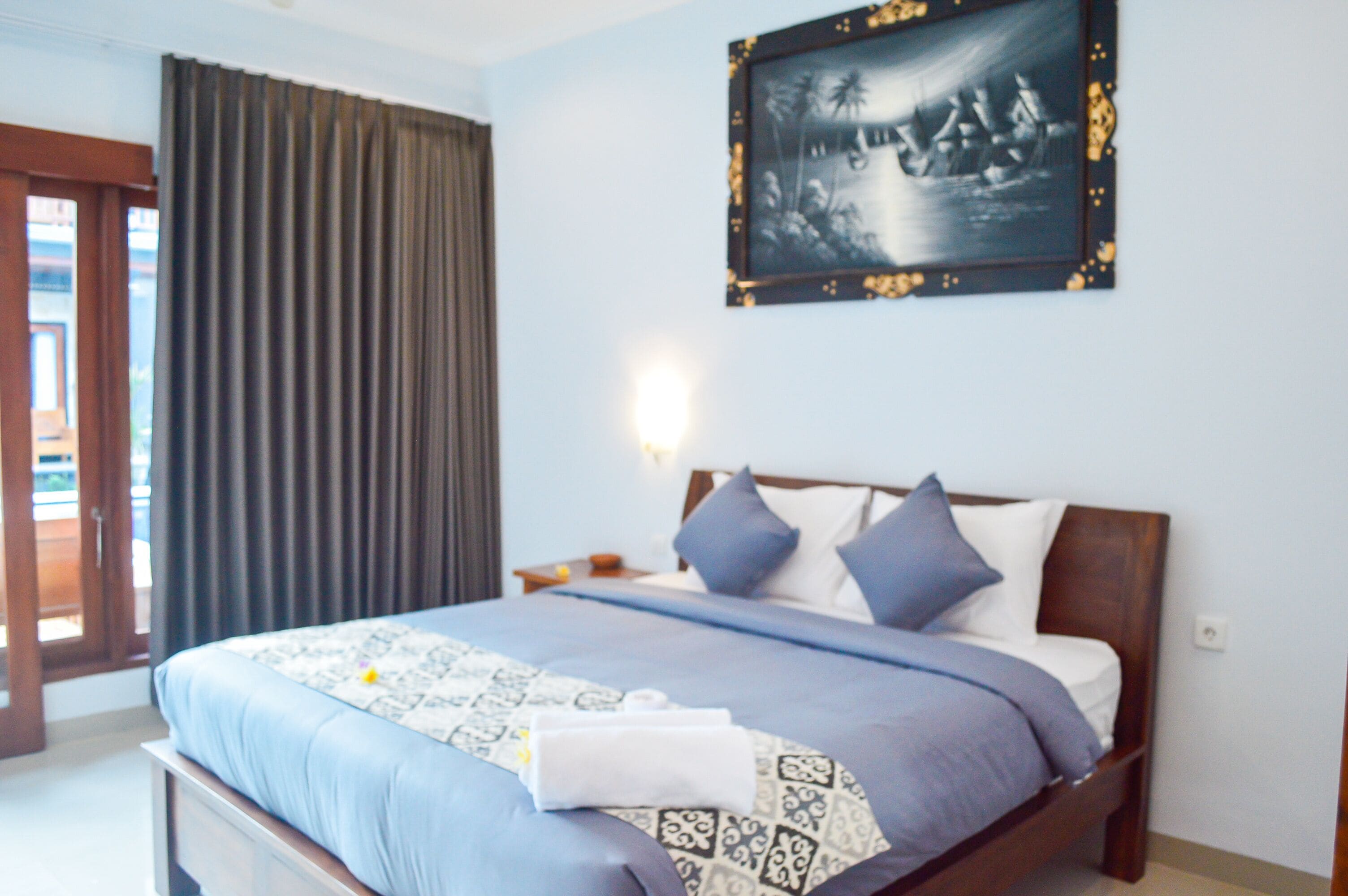 A bedroom with a bed, curtains, a nightstand, and a wall-mounted picture.