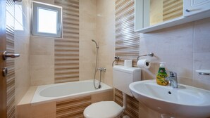 A bathroom with a bathtub, toilet, sink, and a window.