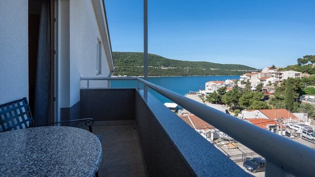 A balcony with a view of a coastal town, a table, and a chair.