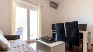 Sala de estar moderna com sofá, mesa de centro e duas cadeiras pretas. Há uma TV em um suporte e uma porta de vidro deslizante que dá para uma área externa.