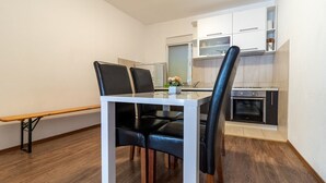Une cuisine moderne avec des armoires blanches, un four encastré et un coin repas comprenant une table blanche et des chaises noires.
