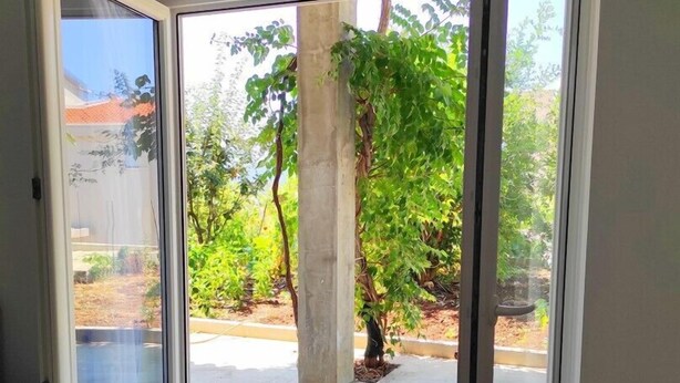 Eine geöffnete Schiebetür führt zu einem Außenbereich mit einer Betonstütze und einem kleinen Baum.