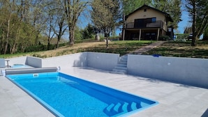 Una piscina rectangular con agua cristalina azul, rodeada por un patio de baldosas y un muro blanco bajo.