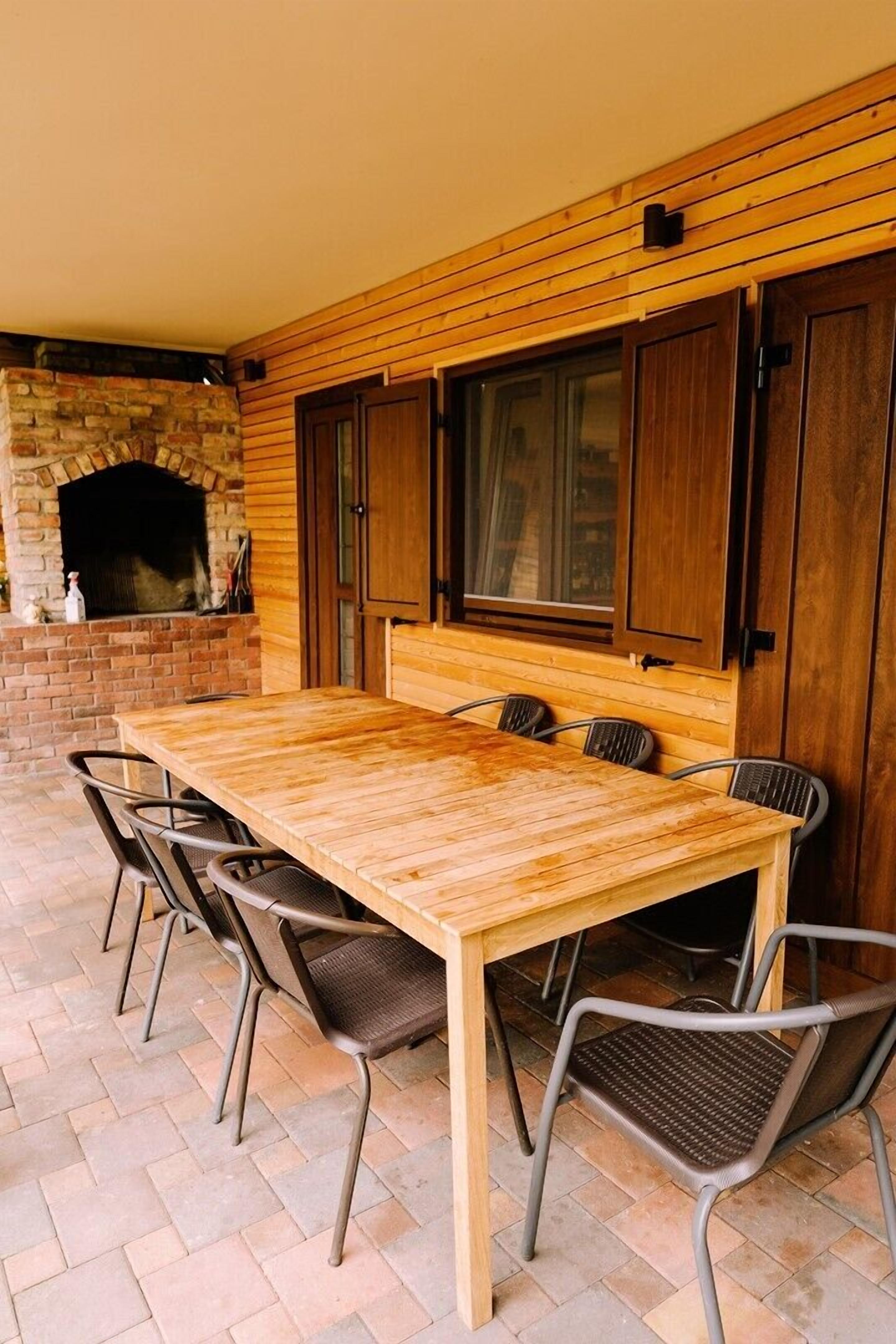 Un'area pranzo all'aperto con tavolo in legno, sedie in metallo, un camino in pietra e pannelli di legno alle pareti.